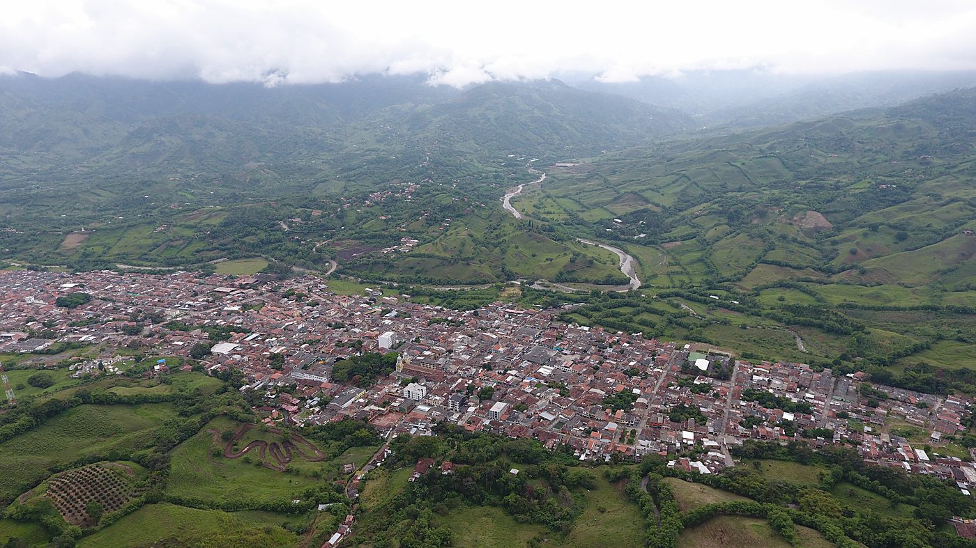 Vista aérea del casco urbano de un municipio de ladera, con su río, las vías y el mosaico de potreros y cultivos alrededor